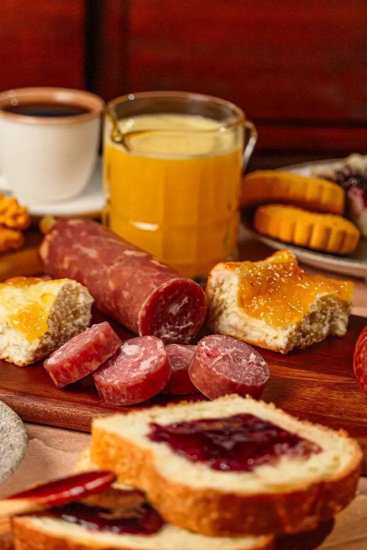 Café da manhã colonial com salame fatiado, pães e geleia